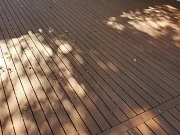 Azek narrow deck with white Trademark railing surrounded by green trees and a bright blue sky, conveying a sense of relaxation and craftsmanship